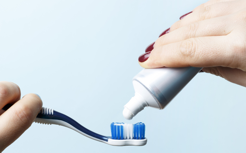 female hand holding a toothbrush and squeezing toothpaste