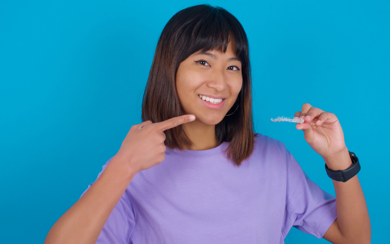 young woman holding invisible aligner pointing her perfect straight teeth