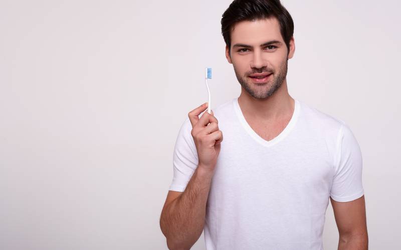 smiling-man-brushing-his teeth with a toothbrush on white background